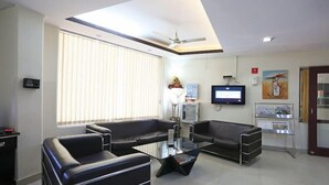 A modern waiting area with leather sofas, a glass coffee table, a ceiling fan, a television, and a wall-mounted information board. - Plazzo (New Delhi)