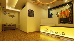 A reception area with a wooden floor, a sofa with cushions, a wall-mounted sign, and a painting. - Plazzo (New Delhi)