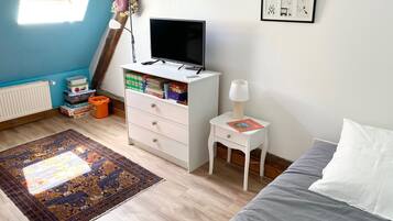 Een slaapkamer met een bed, een bureau met een computer, een boekenplank, een raam met zonwering en een radiator.