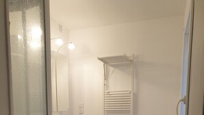 Un bagno con pavimento in legno, sanitari bianchi, un lavabo con specchio, un water e una zona doccia.