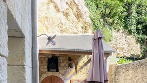 Patio esterno con pareti in pietra, tavolo e sedie in legno, ombrellone e una porta rustica.