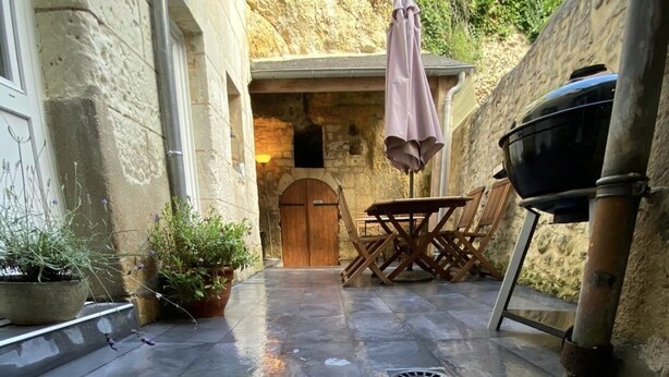 Patio esterno con pareti in pietra, una porta in legno, un tavolo con sedie e un barbecue.
