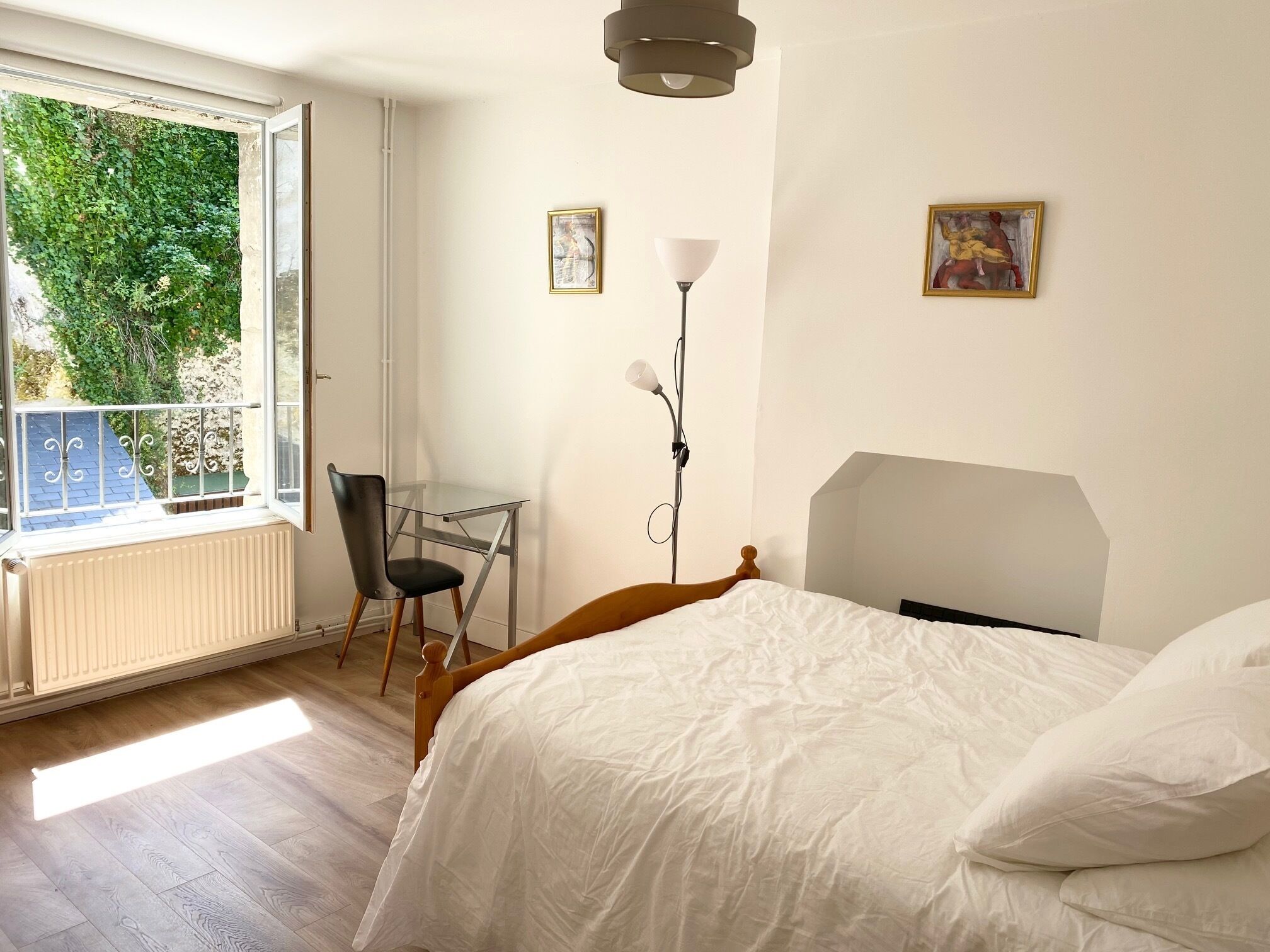 A bedroom with a bed, a desk, a chair, and a window with a view of greenery.