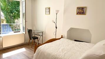 A bedroom with a bed, a desk, a chair, and a window with a view of greenery.