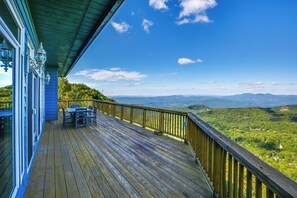 Terraza de madera con mesa y sillas, con vistas a un paisaje montañoso.