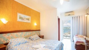 Habitació d'hotel amb llit, una taula de nit, llum penjada a la paret, quadre amb marc i balcó amb cortines.