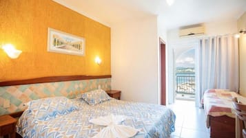Quarto de hotel com cama, mesa de cabeceira, luminária na parede, quadro emoldurado e varanda com cortinas.