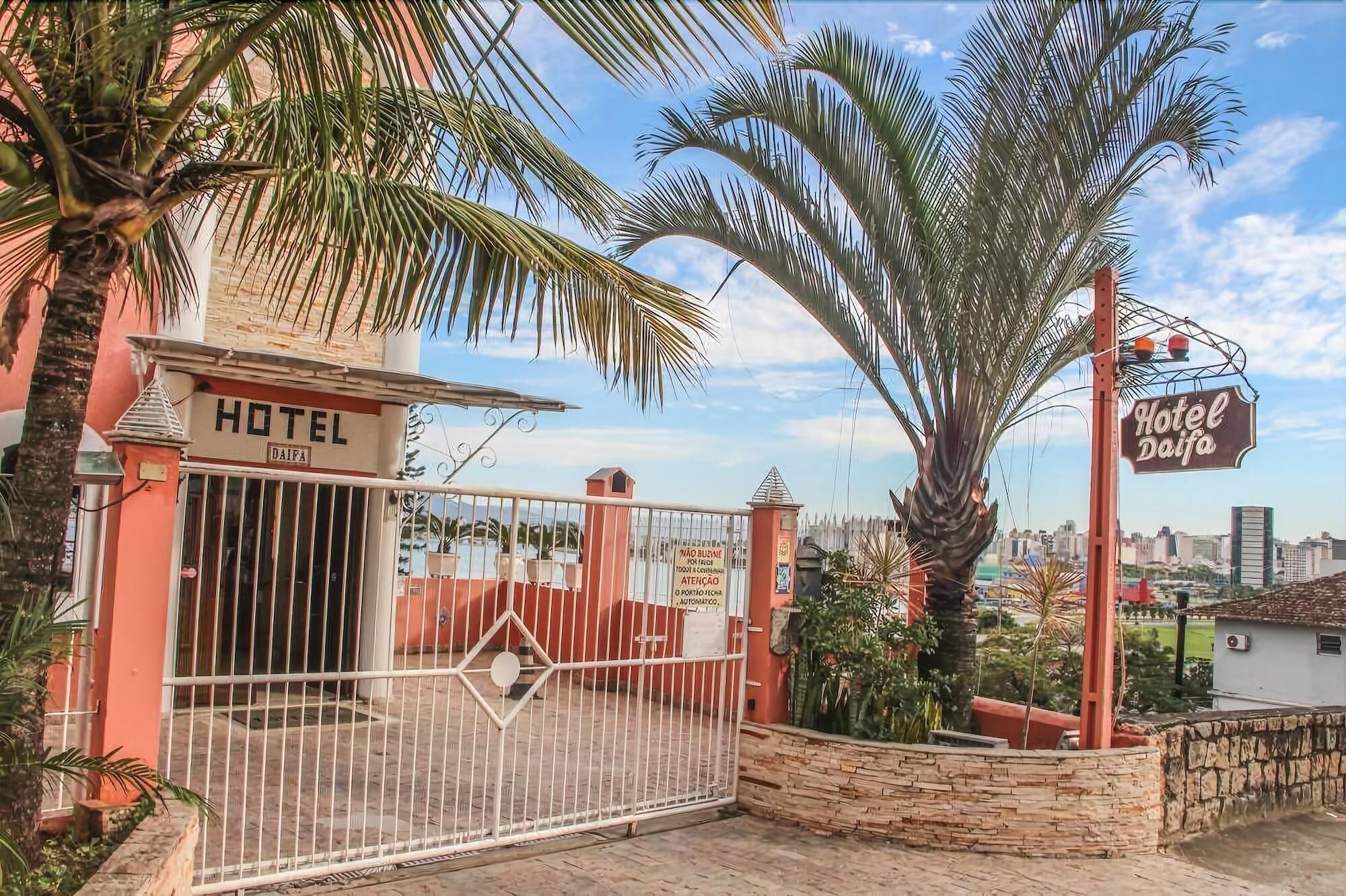 A hotel entrance with a gated driveway, palm trees, and a cityscape in the background.