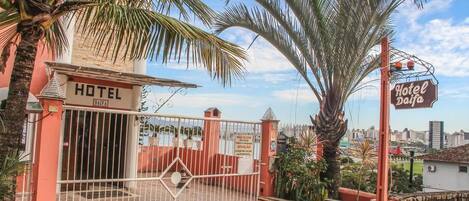 A hotel entrance with a gated driveway, palm trees, and a cityscape in the background.