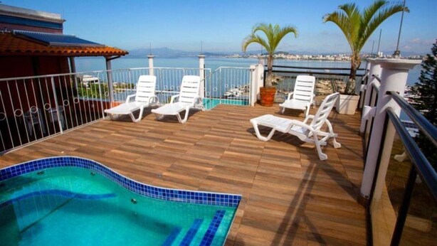 Una terrassa de fusta amb una piscina, gandules blanques i vista al mar.