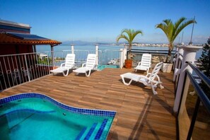A wooden deck with a swimming pool, white lounge chairs, and a view of the sea. - Hotel Daifa (Florianópolis)