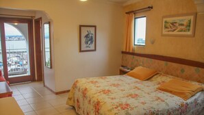 Habitació d'hotel amb un llit, una finestra amb cortines, una porta que dona a un balcó i un quadre al mur.