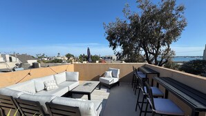 A rooftop patio with outdoor furniture, a view of the city, and a large tree.