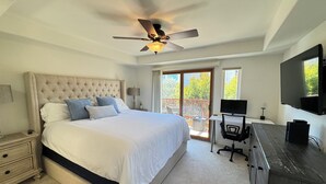 A bedroom with a bed, a desk, a chair, a ceiling fan, and a TV.