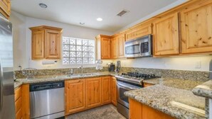 A modern kitchen with wooden cabinets, granite countertops, stainless steel appliances, and a window with a decorative grid pattern.