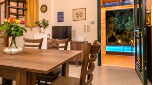 Un'area pranzo con un tavolo e sedie in legno, un vaso con fiori, un orologio, una televisione e vista su una piscina esterna illuminata di notte.