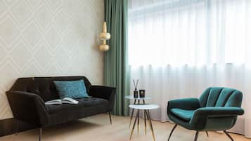 Een moderne woonkamer met een zwarte bank, een blauwgroene fauteuil en een kleine ronde tafel met een boek en een kaars.