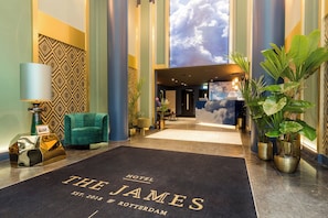 A hotel lobby with a reception desk, a green armchair, potted plants, and a large wall mural. - The James Hotel Rotterdam (Rotterdam)