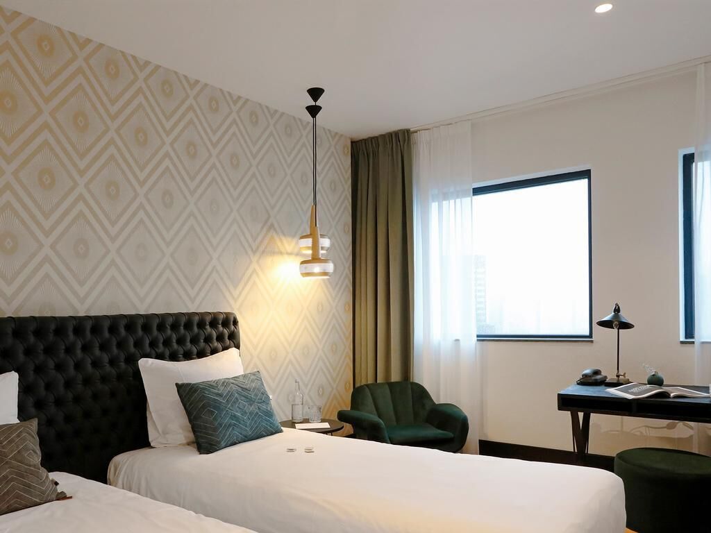 A hotel room with two beds, a desk, a chair, and a large window.