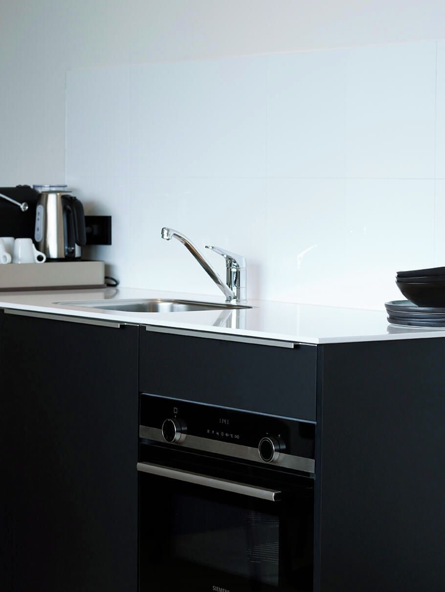 A modern kitchen with a stainless steel sink, a built-in oven, and a coffee machine.