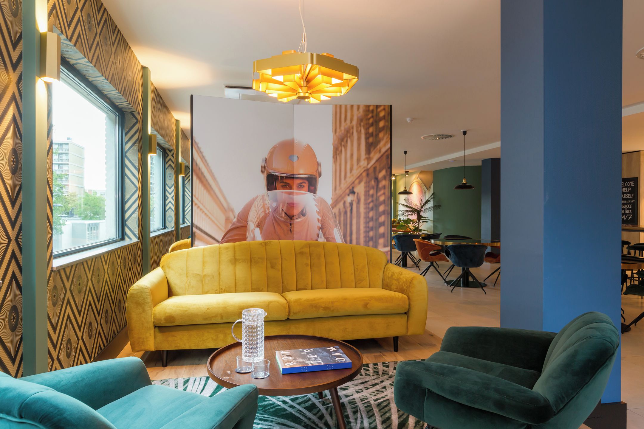 A modern interior with a yellow sofa, green armchairs, a coffee table, and a large poster on the wall.