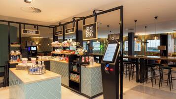 A modern coffee shop with a self-service kiosk, a counter with various items, and a seating area with bar stools.