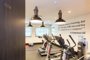 Ein Fitnessraum mit Trainingsgeräten, einem motivierenden Zitat an der Wand und einem Wasserspender.