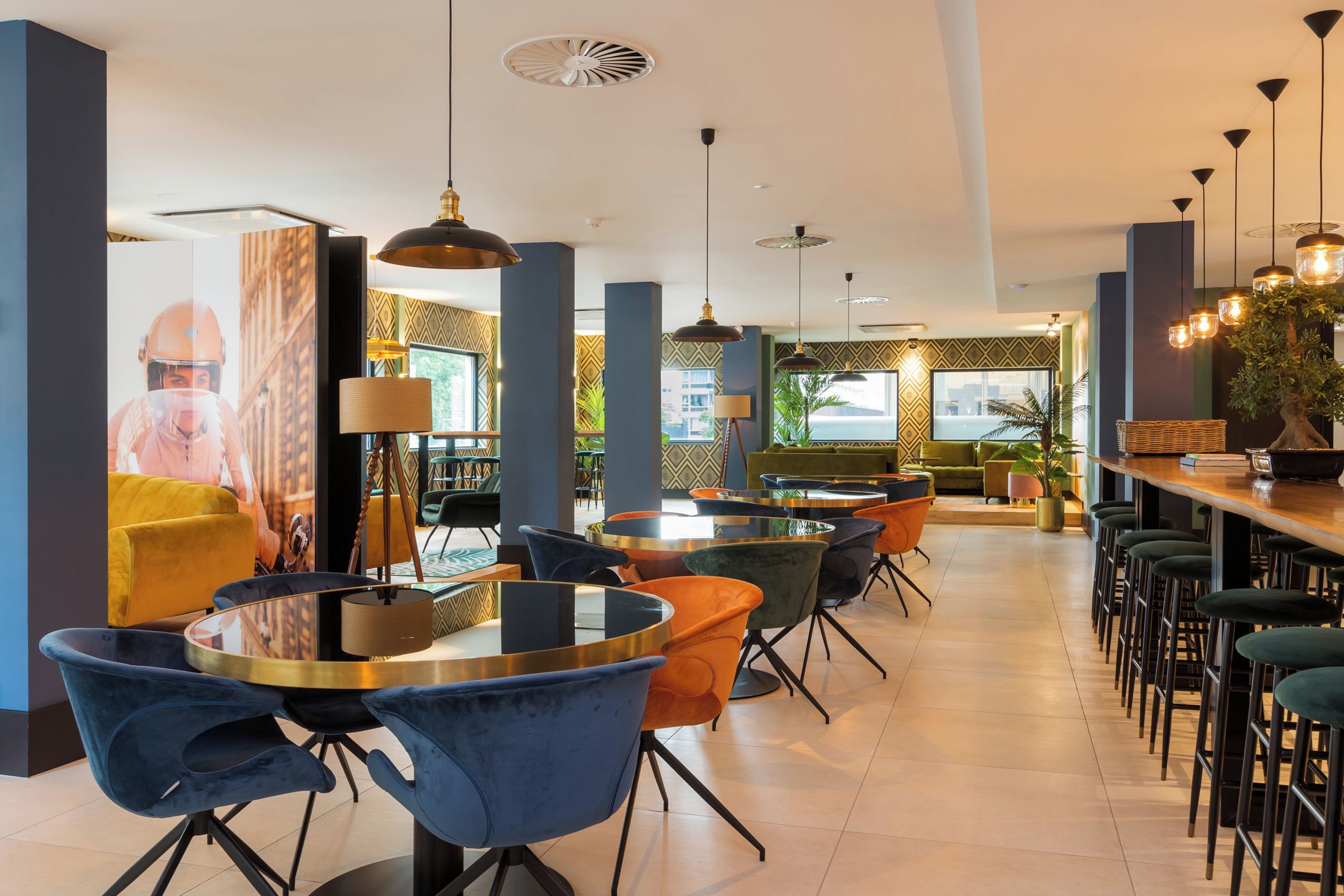 A modern restaurant with round tables, bar stools, and pendant lighting.