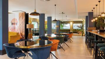A modern restaurant with round tables, bar stools, and pendant lighting.