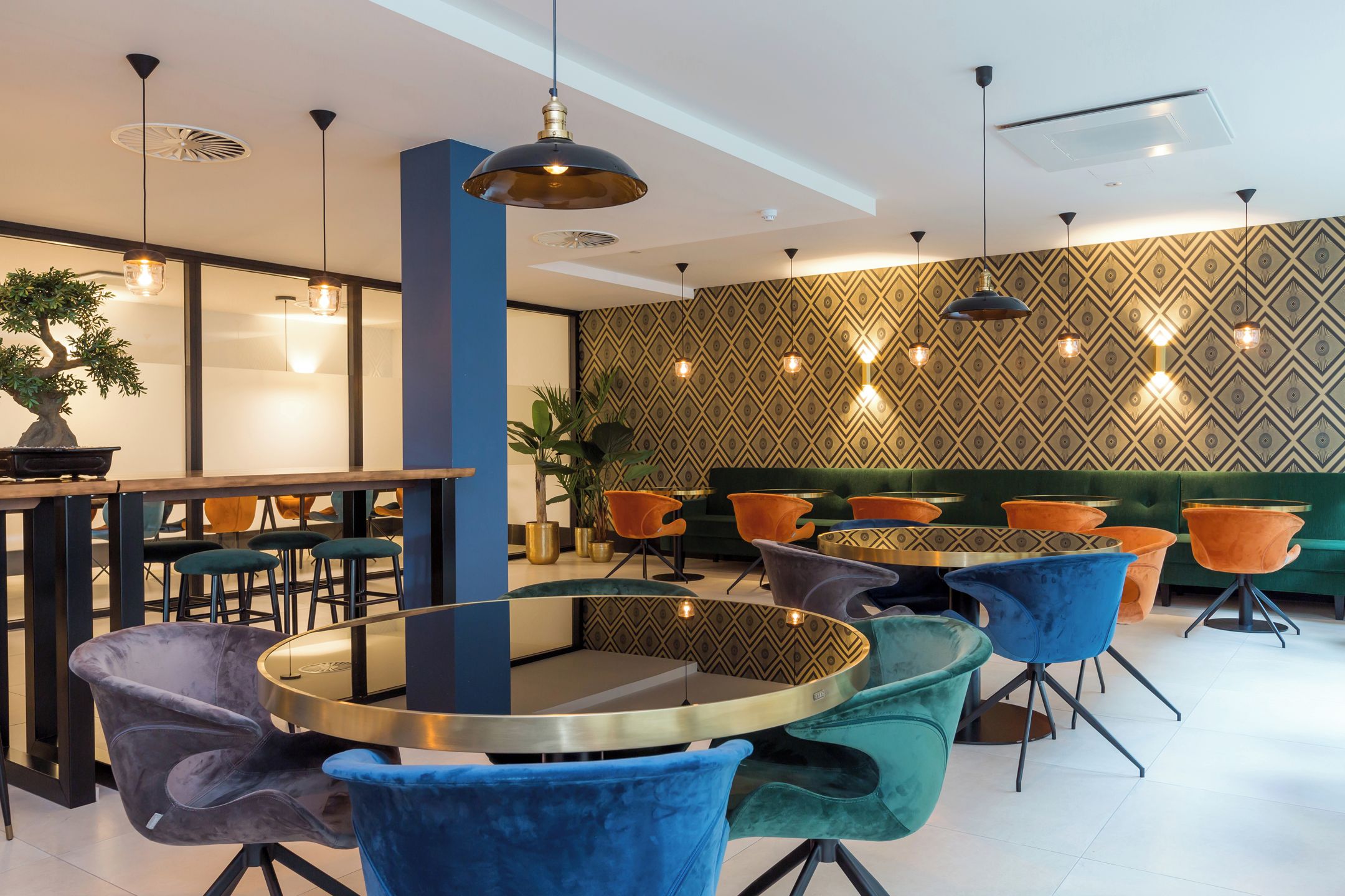 Een modern interieur met ronde tafels, kleurrijke stoelen en behang met een patroon.