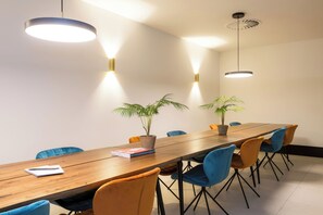 A conference room with a long wooden table, blue and orange chairs, two potted plants, and pendant lighting. - The James Hotel Rotterdam (Rotterdam)