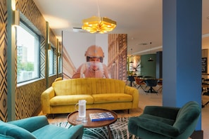 A modern interior with a yellow sofa, green armchairs, a coffee table, and a large poster on the wall. - The James Hotel Rotterdam (Rotterdam)