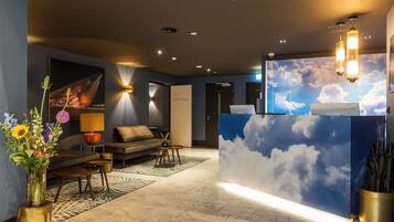 A lobby with a reception desk, a sofa, a coffee table, a vase with flowers, and a wall with a cloud mural.