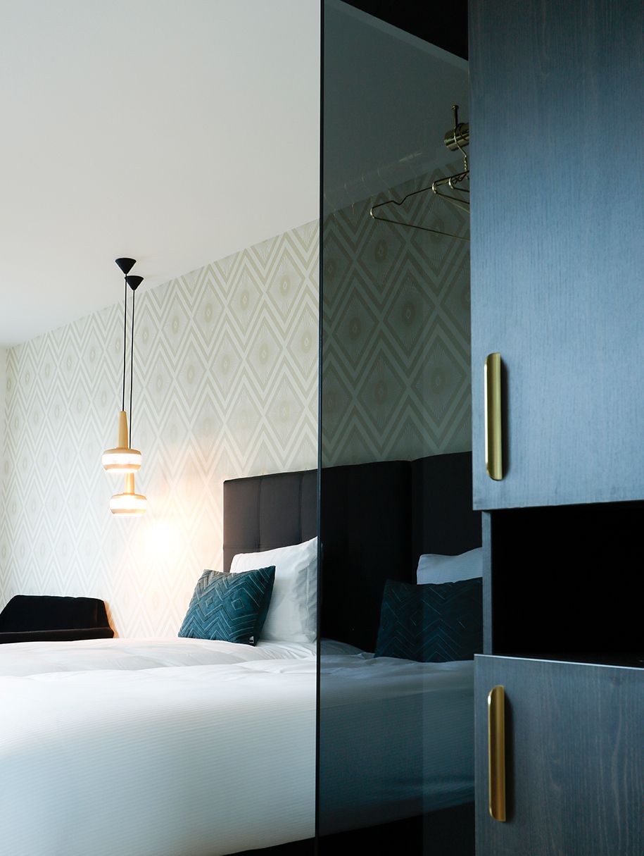 Een moderne slaapkamer met een bed, een hanglamp en een garderobe met een metalen handgreep.