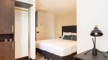 A modern hotel room with a bed, bedside table, lamp, and wardrobe.