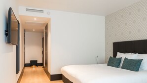 A modern hotel room with a large bed, a flat-screen TV mounted on the wall, and a patterned wallpaper on the wall behind the bed. - The James Hotel Rotterdam (Rotterdam)