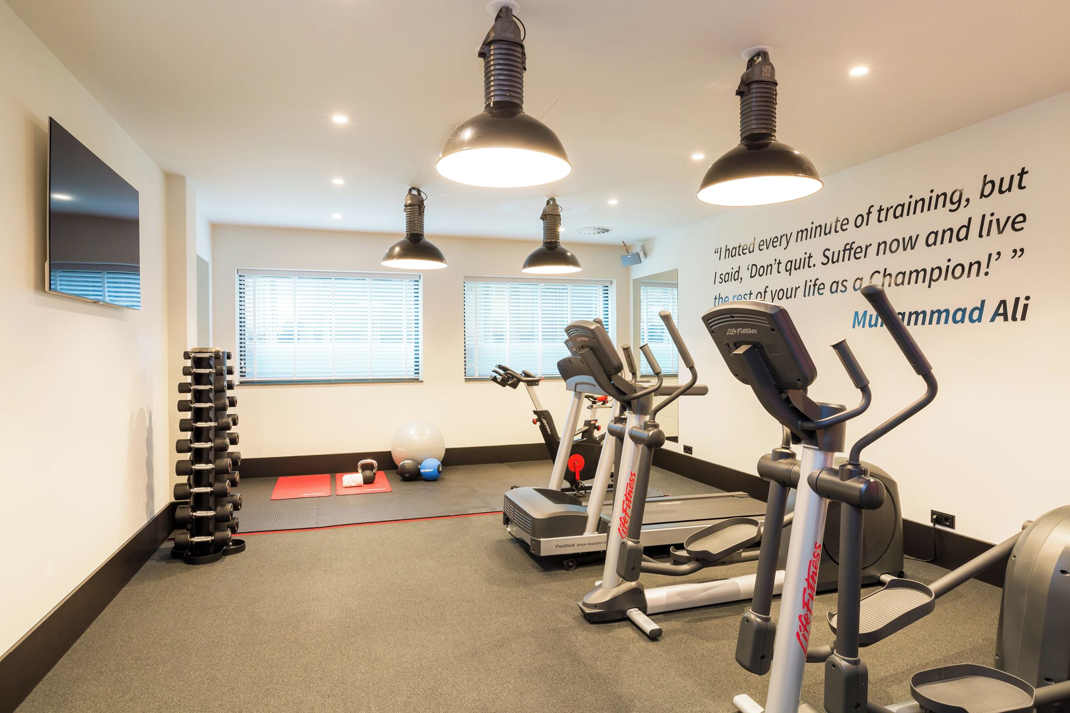 A gym with treadmills, elliptical machines, and a wall with motivational quote.