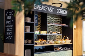 A breakfast corner with a sign reading 'WELCOME HELP YOURSELF TO BREAKFAST SNACKS & DRINKS 24/7'. - The James Hotel Rotterdam (Rotterdam)