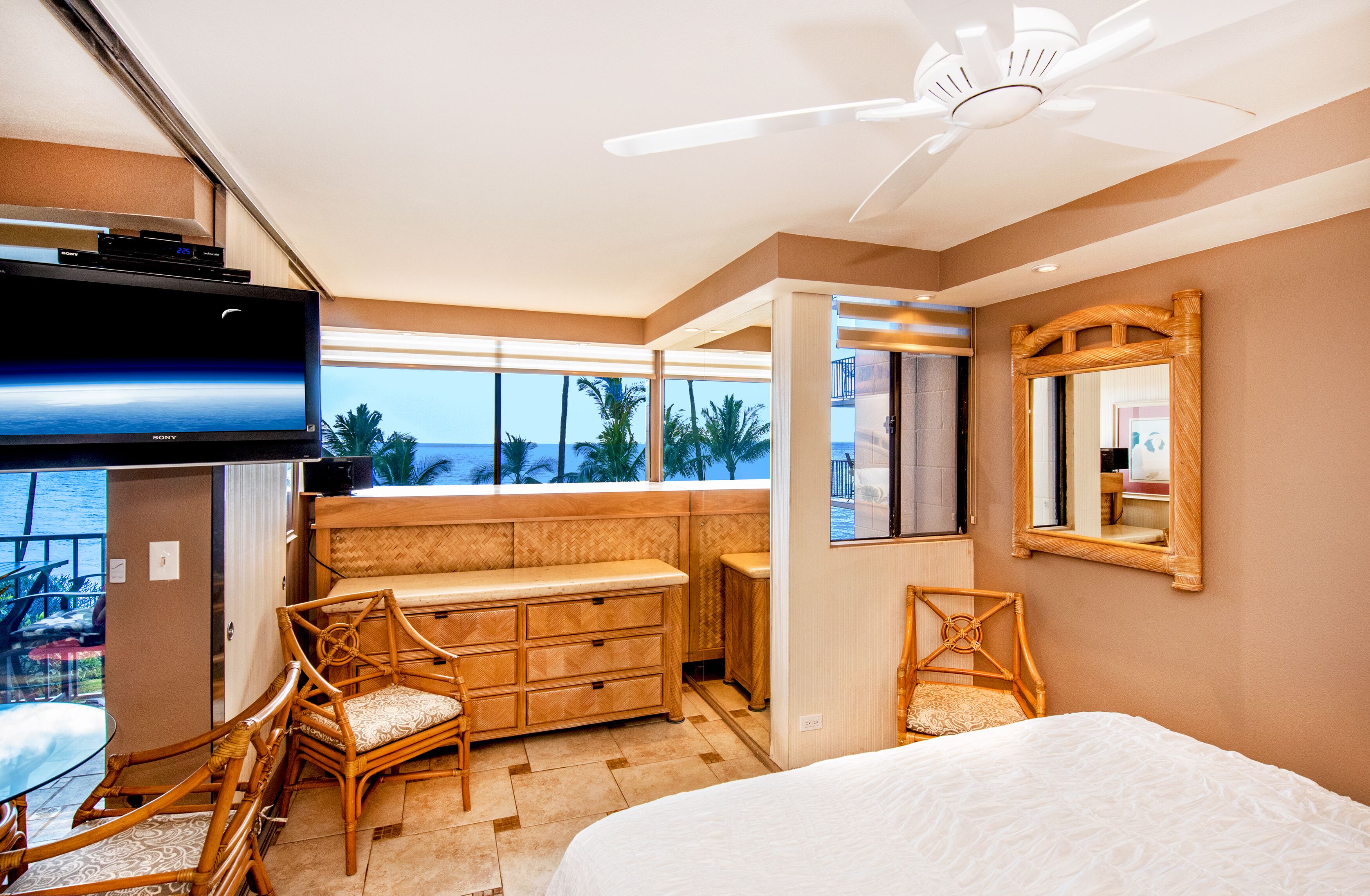 Ein Hotelzimmer mit Balkon, einem Bett, einem Fernseher und einem Deckenventilator.