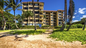 A multi-story hotel with balconies, surrounded by palm trees and a sandy beach area. - Kealia 402 Oceanfront Condo and Beautiful Secluded White-Sand Sugar Beach (Kihei)