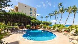 A pool area with lounge chairs, a clear blue pool, and a view of the ocean. - Kealia 406 Oceanview Condo on Splendid Sugar Beach and Stroll the Beach (Kihei)