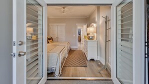 Un couloir menant à une chambre à coucher équipée d’un lit, d’une commode et d’une lampe.