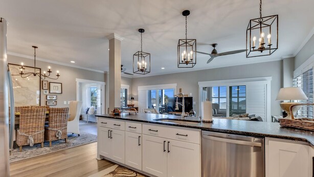 Une cuisine moderne avec des armoires blanches, des appareils en acier inoxydable et un grand îlot central. On y trouve des luminaires suspendus et un ventilateur de plafond.