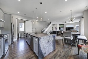 A modern kitchen with a marble island, stainless steel appliances, and a dining area with a piano.