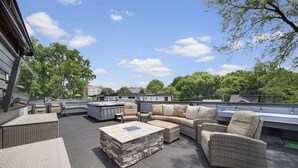 A rooftop patio with outdoor furniture, a hot tub, and a stone fireplace.