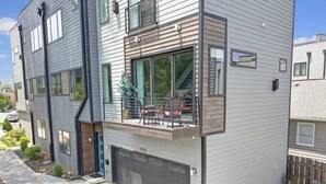 A modern two-story residential building with a garage, a balcony with outdoor seating, and a clear view of the surrounding neighborhood.