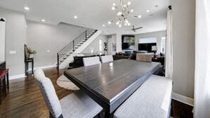 A spacious dining area with a large table, modern lighting, and a staircase leading to an upper level.
