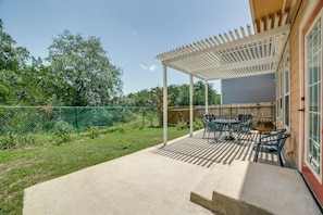Un porche cubierto con mobiliario exterior, una pérgola y vistas a un patio trasero con valla y árboles.