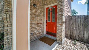 A brick house with a red door, a wooden fence, and a doormat.