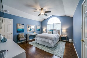 Un dormitorio con cama, escritorio, silla, ventilador de techo y ventana con persianas.